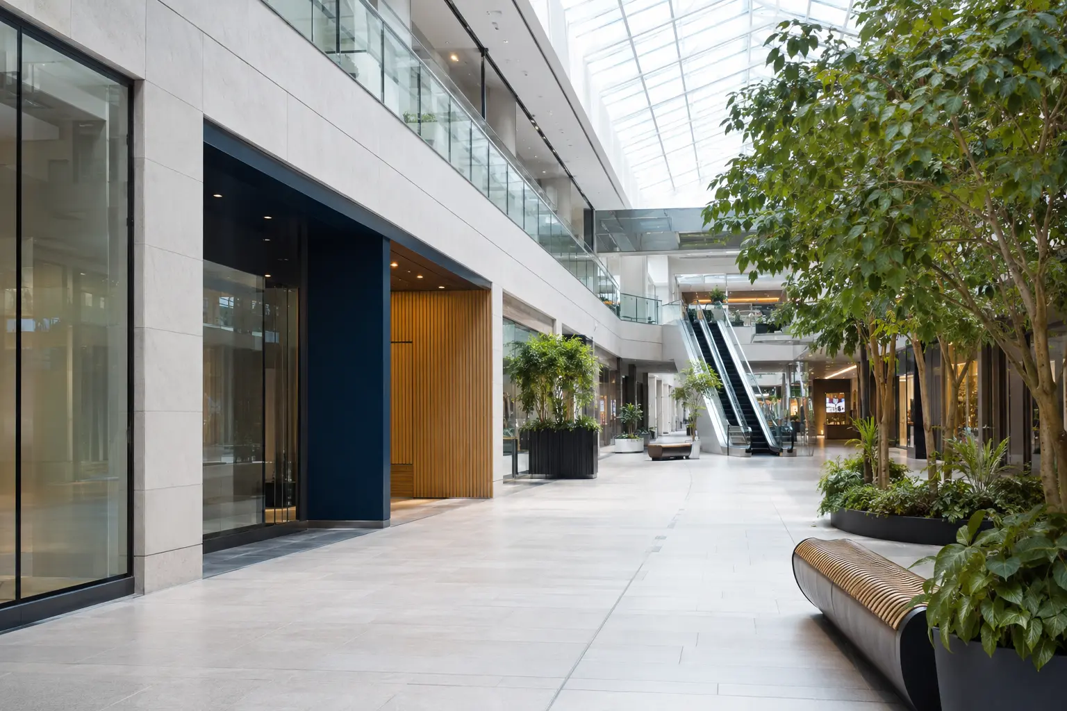 Bright modern shopping centre concourse with storefronts, seating, escalators and clear public sightlines.